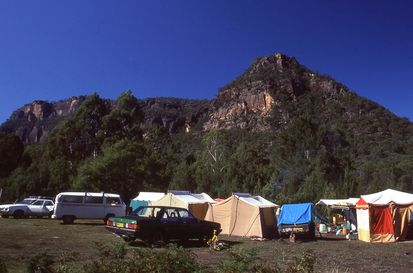 Tents and vehicles at a bush campground beneath sandstone cliffs